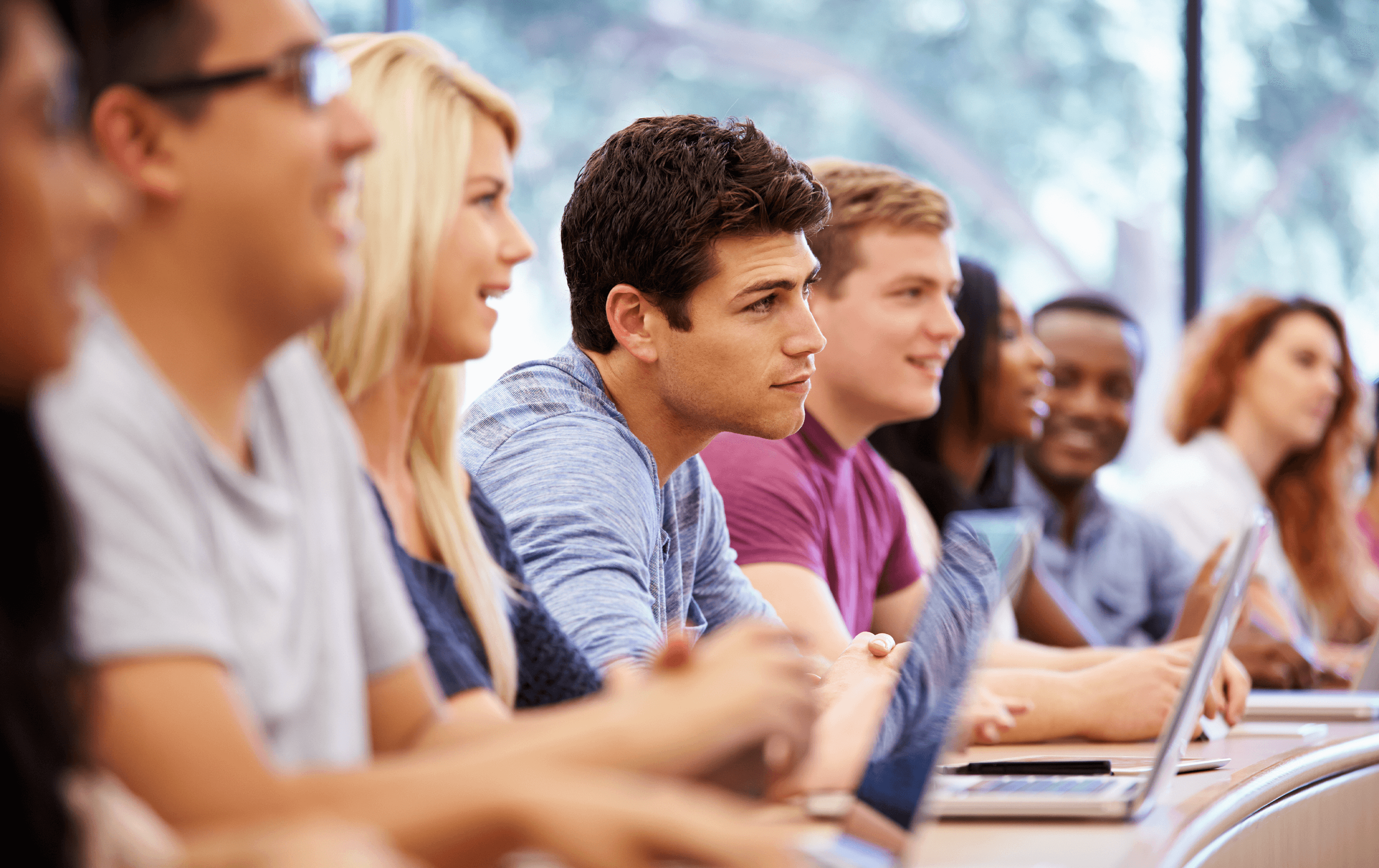 students sitting at a long desk listening to speaker