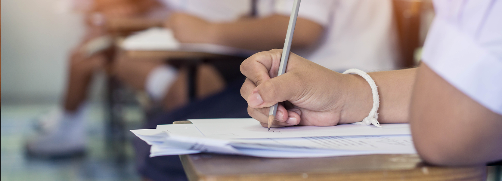 student writing on paper with pencil at desk