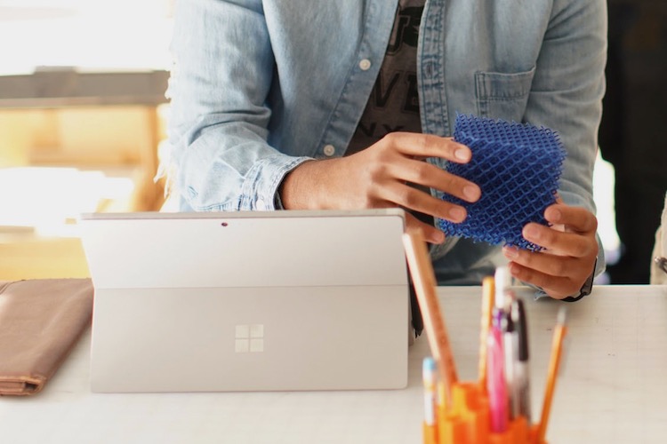 A student holding a cube in front of a laptop.