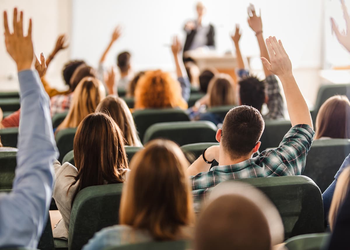 Group of students from back raising hands.