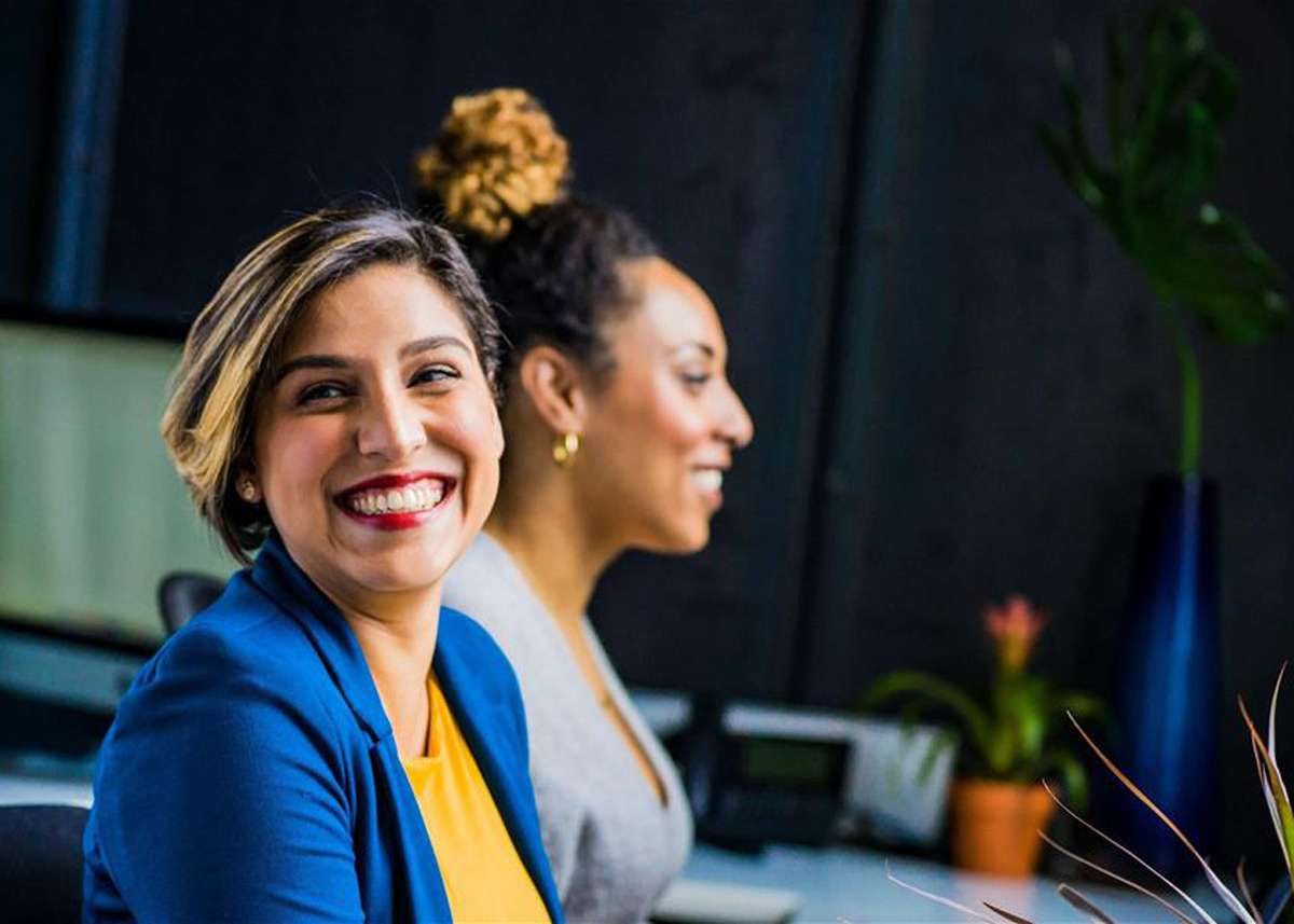 two women smiling and sitting at computers