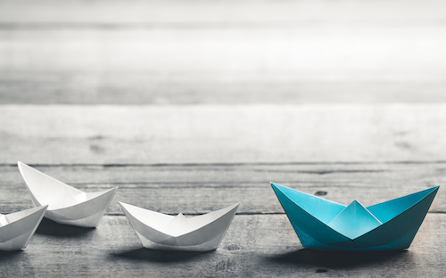 multiple paper boats, white ones following a larger blue one