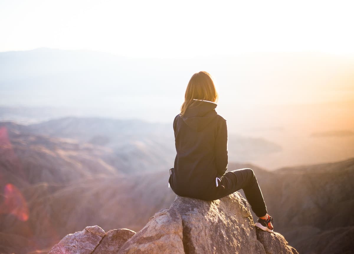 person sitting on rock facing mountains