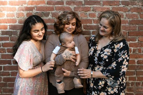 Three women with infant in front of brick wall