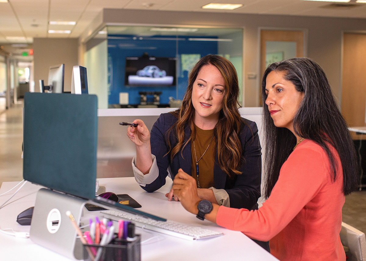 two women talking and working on a computer