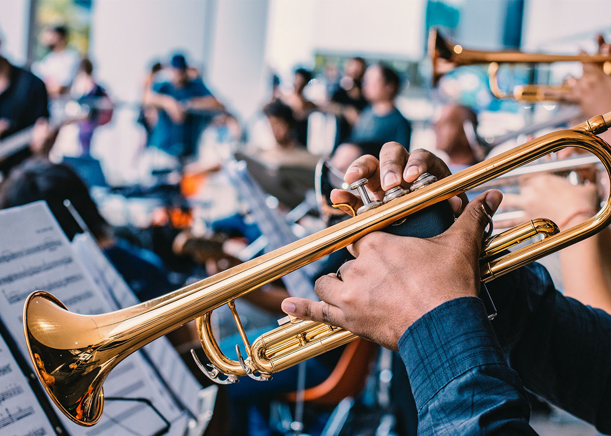 Close up of a person playing a trumpet in a room with a large band