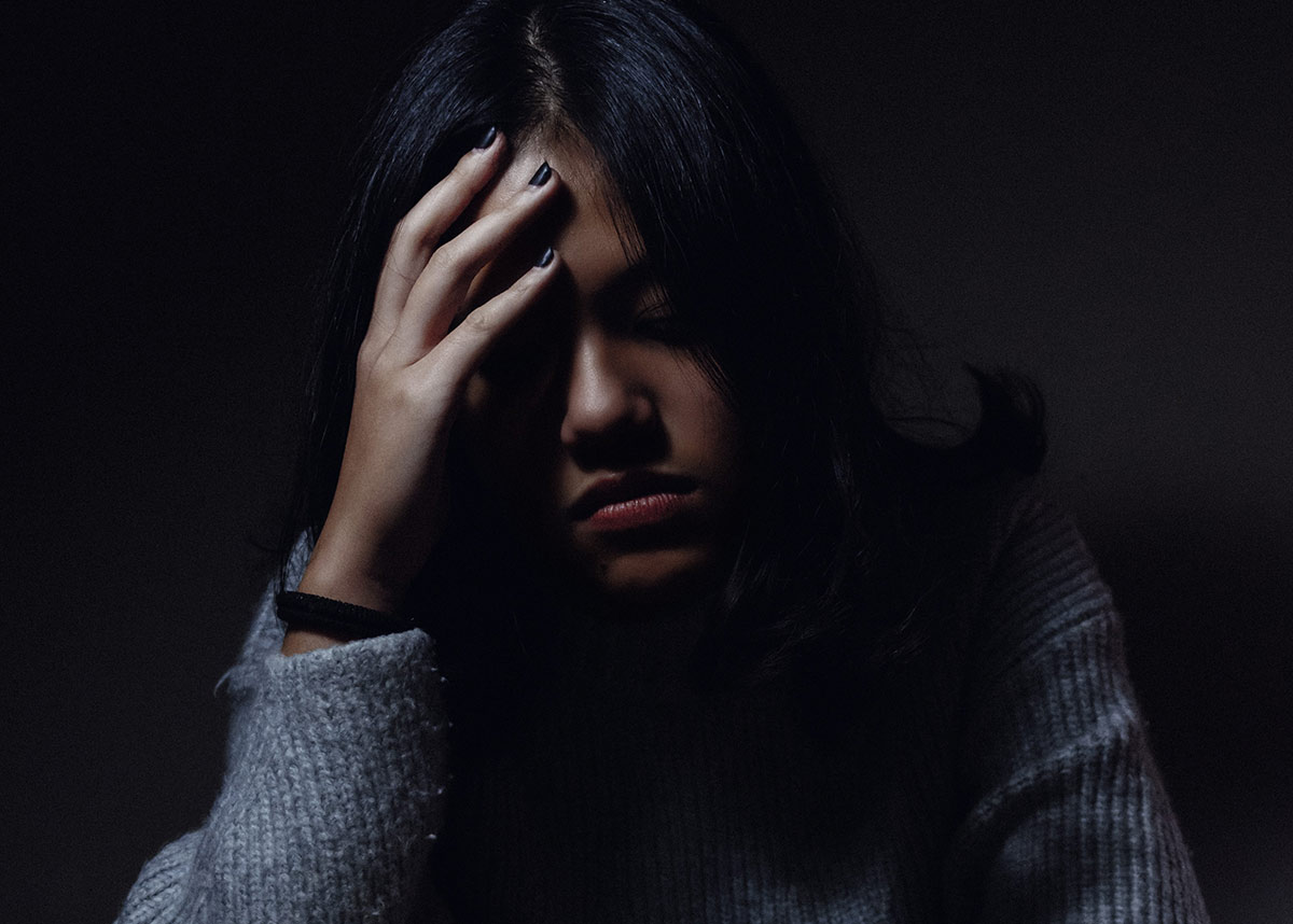 woman sitting in the dark with her hand on her head