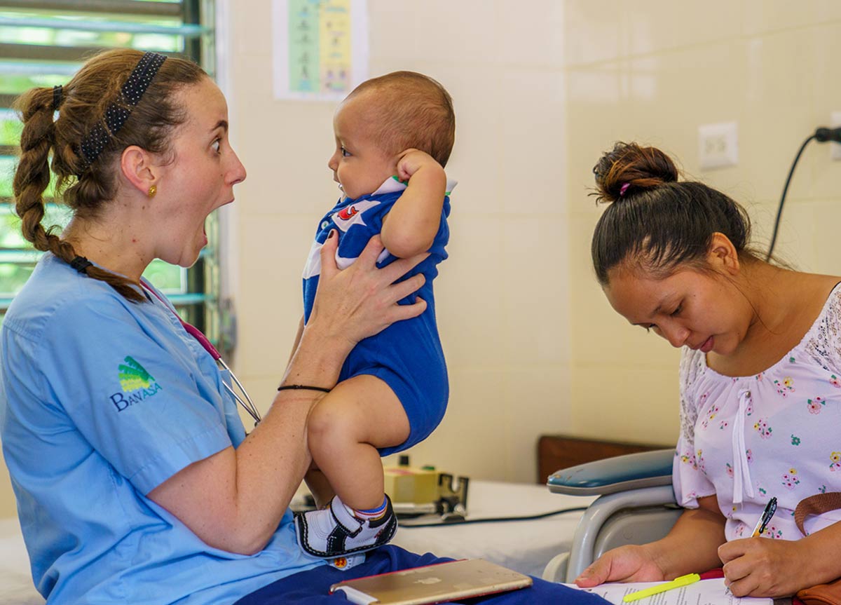 Student holding baby while mom fills out paperwork