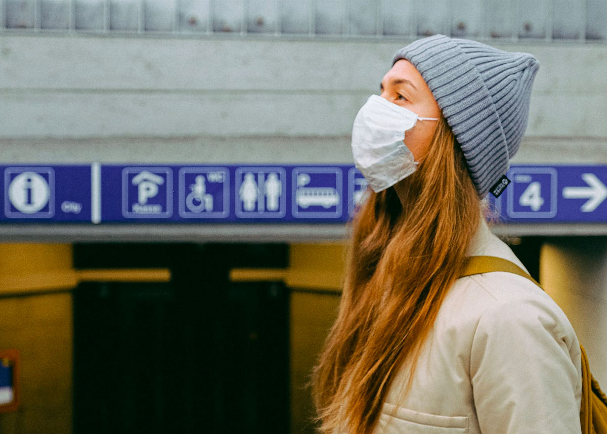 Person wearing mask outdoors, standing near subway entrance