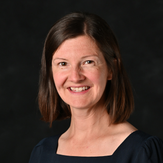 Woman smiling in headshot wearing dark shirt on dark background