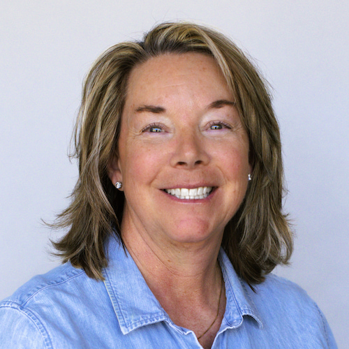 White woman smiling at camera with brown hair and denim button up shirt