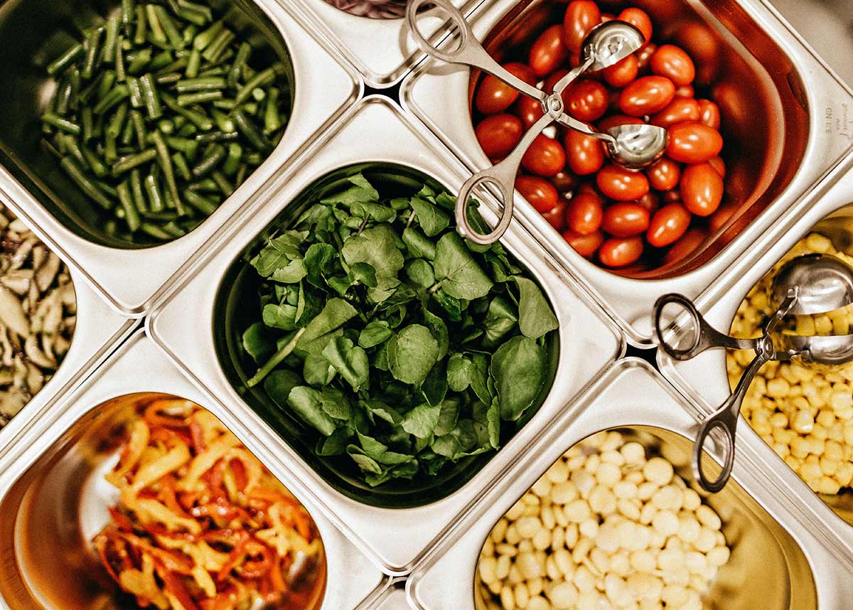 salad bar with different vegetables and tongs