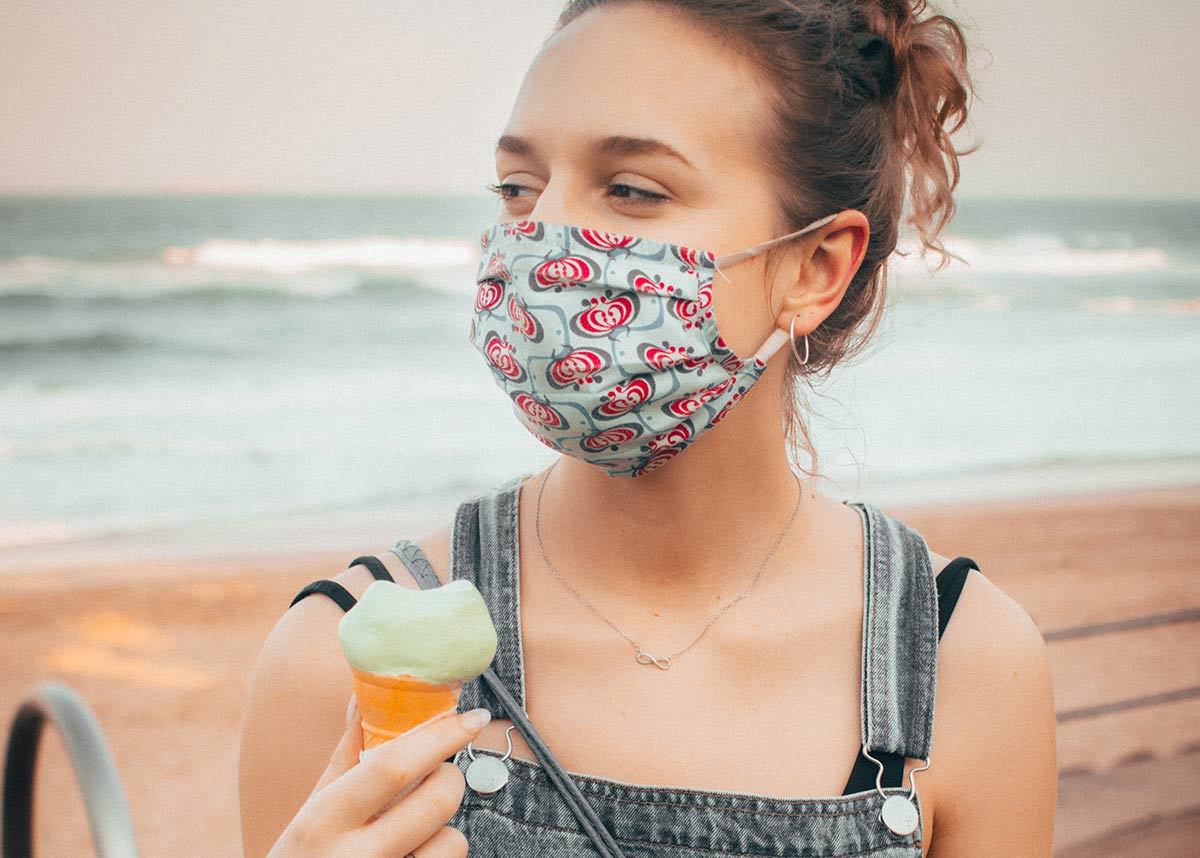 woman wearing a mask at a beach holding an ice cream cone