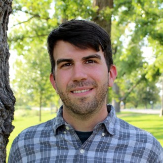 Man smiling in headshot standing outside by a tree