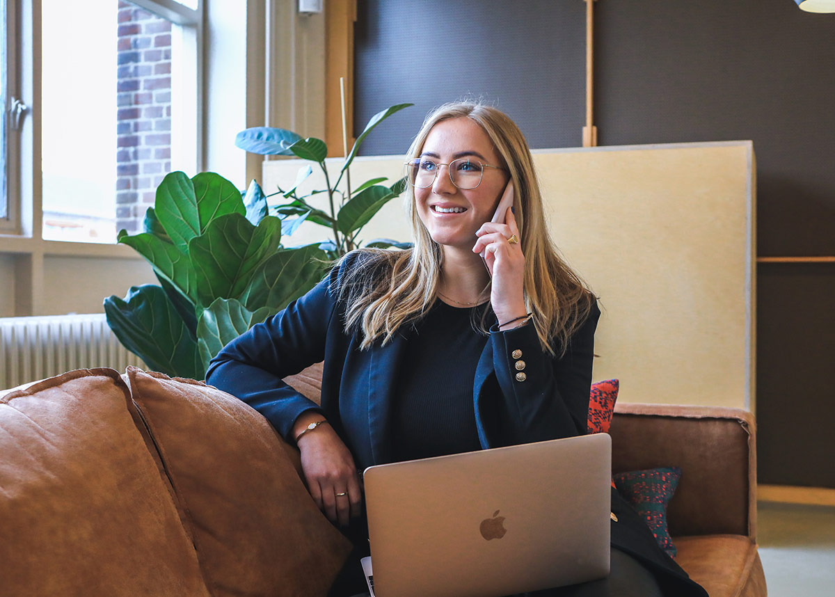 person wearing a blazer smiling on the phone with a laptop in their lap