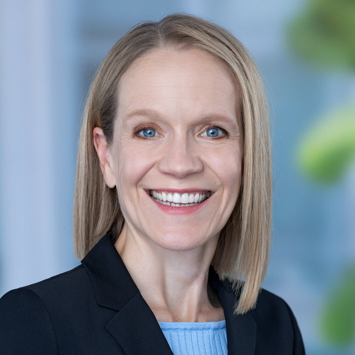 Woman smiling in headshot wearing a dark blazer and light blue shirt