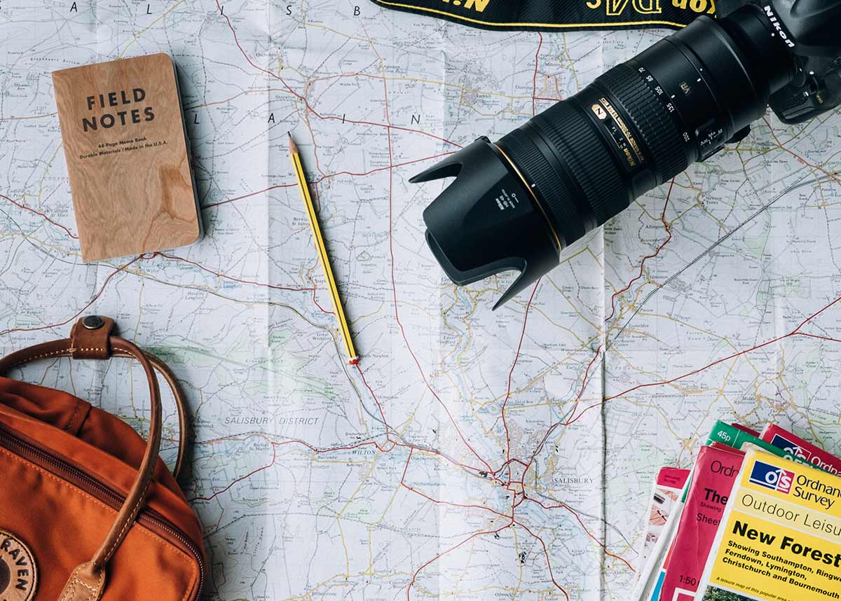 A map with a bag, notebook, camera, and travel guides on top