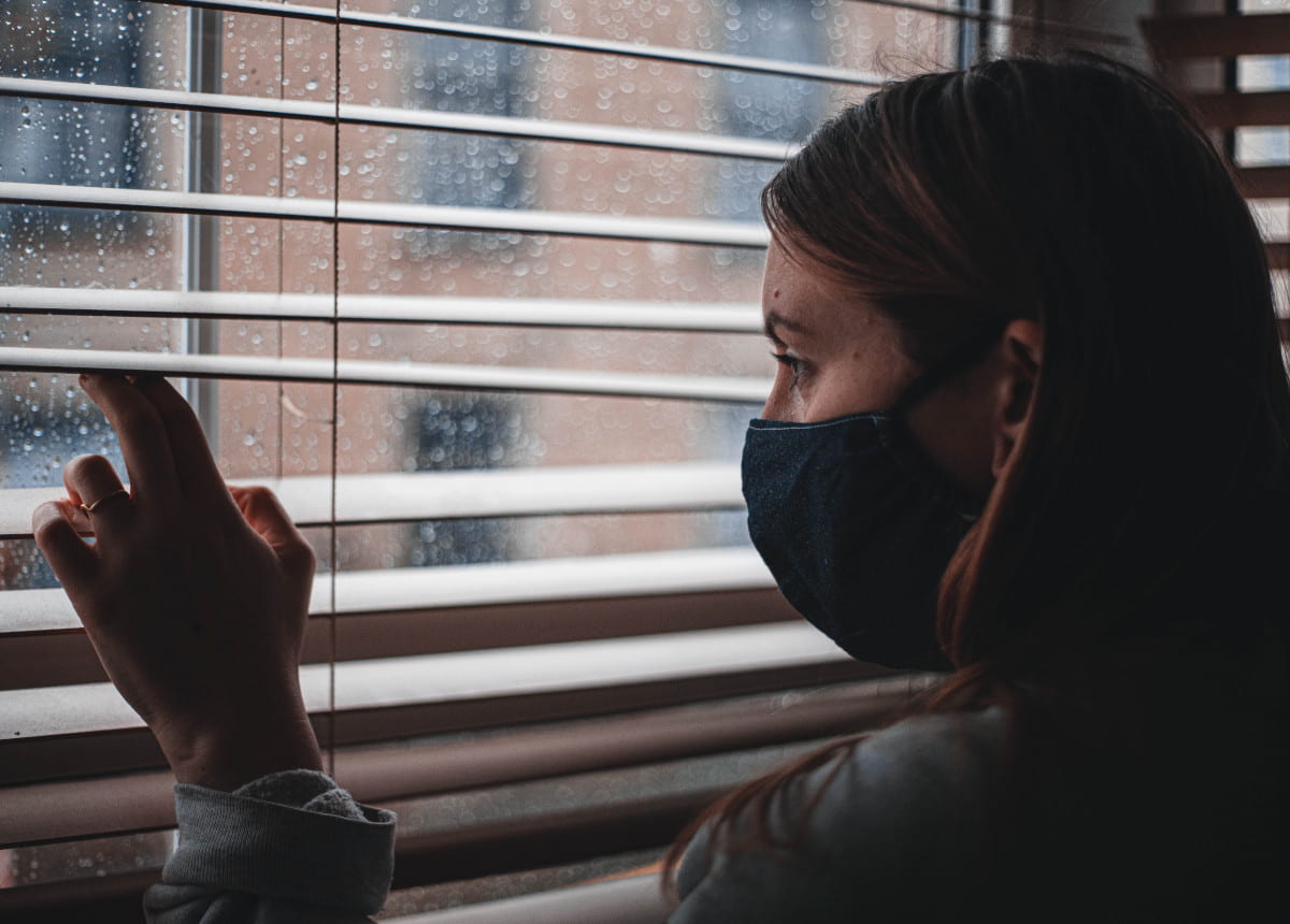 woman wearing mask peering out window