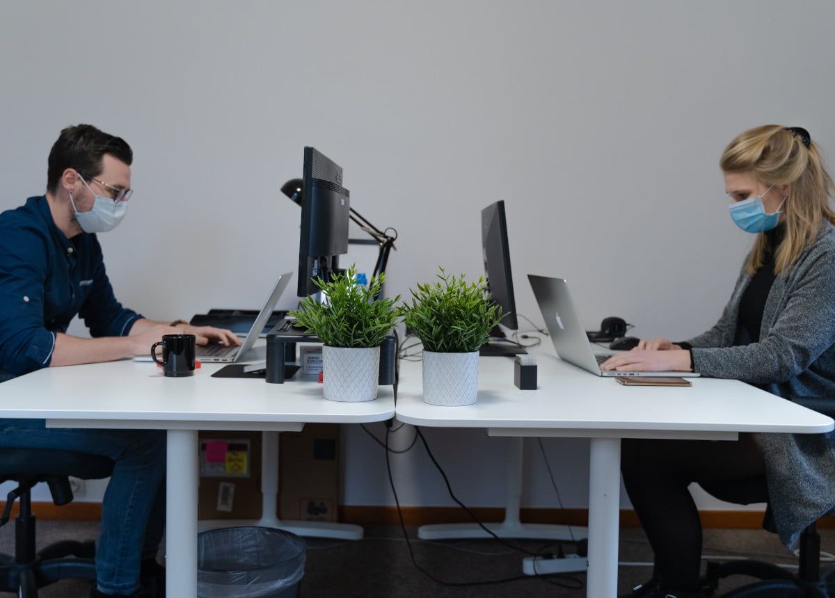 Two people working at a desk area together wearing masks