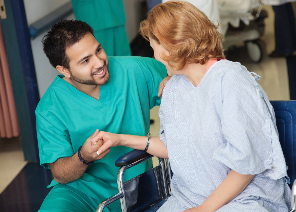 Male nurse kneeling down by woman patient in wheelchair