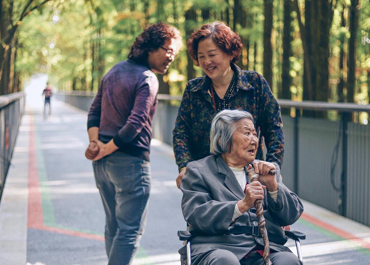 older adult in wheelchair with person pushing them in a park