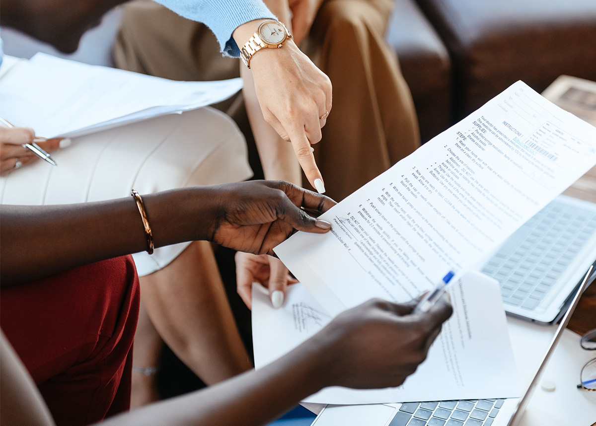 Close up of person holding research paper, others in the space discussing paper, pointing