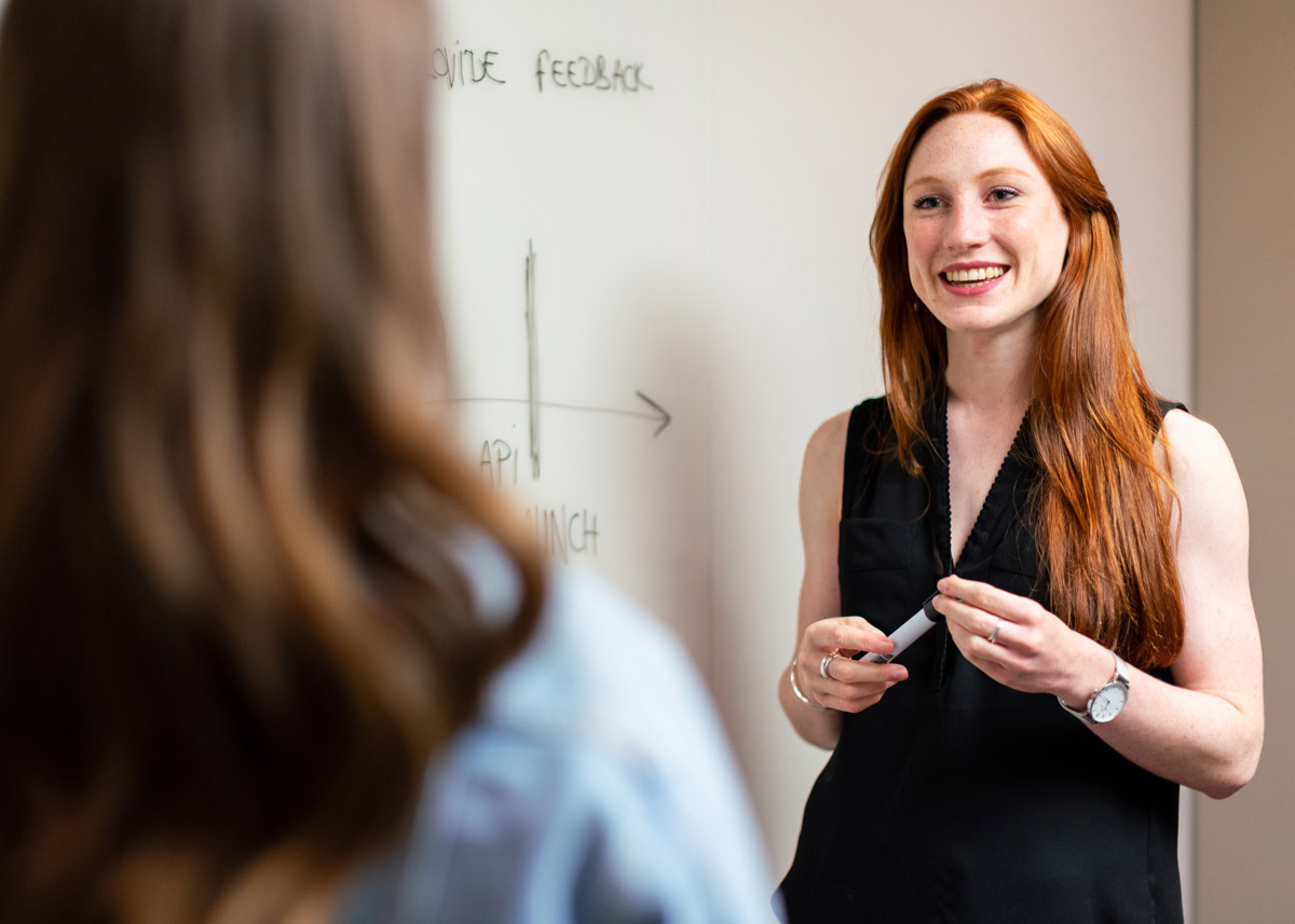 woman smiling and holding a marker in front of a white board