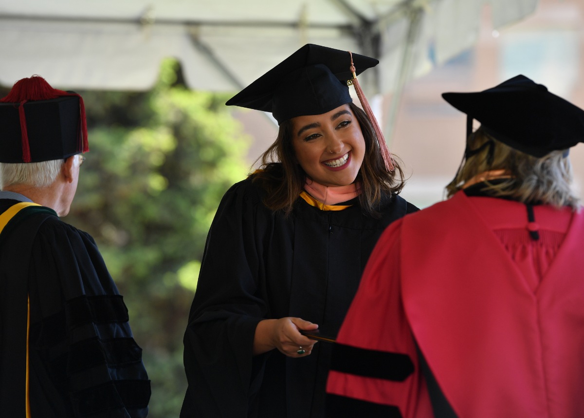 ColoradoSPH grad in cap and gown smiling while receiving diploma