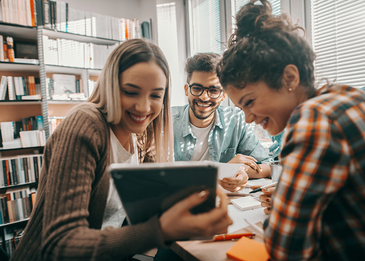 three students laughing and looking at an ipad