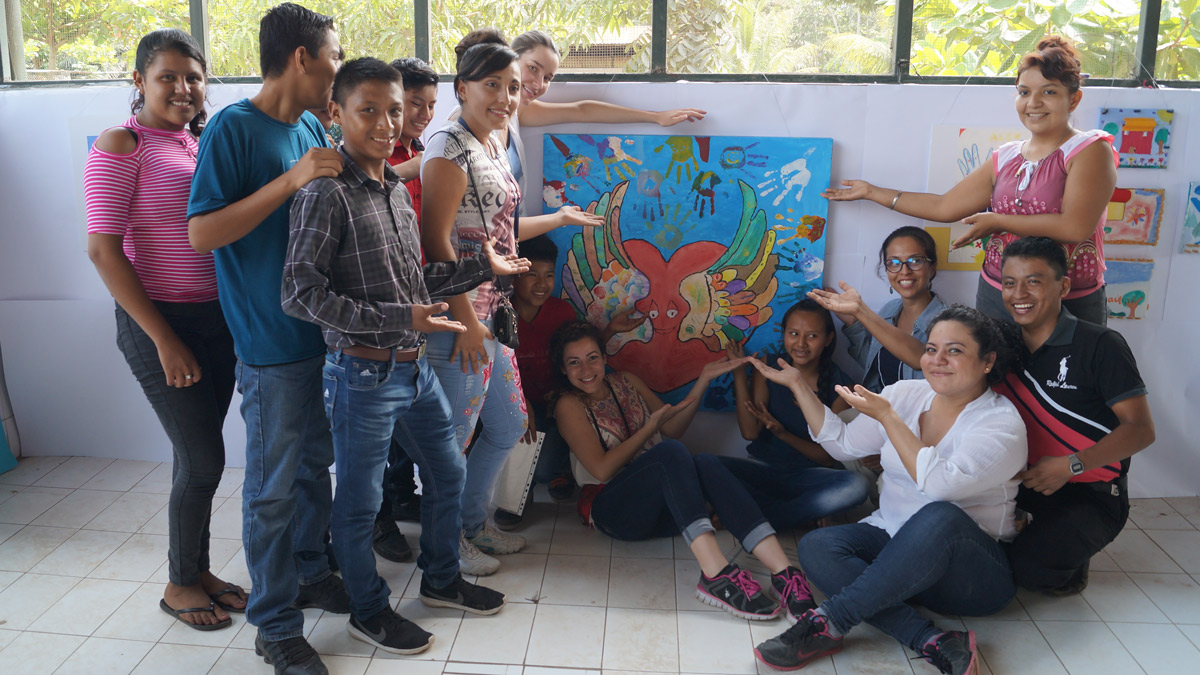 group of people smiling standing around a painting