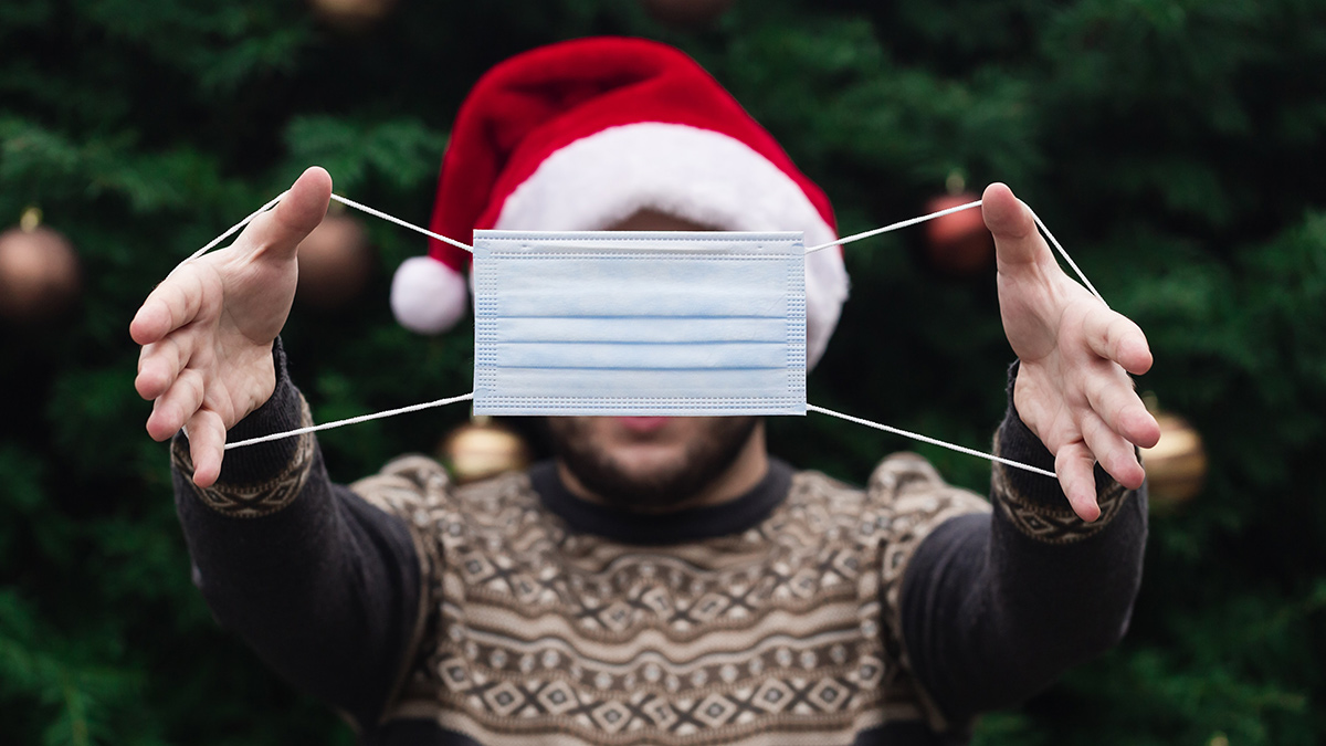 man in a santa hat holding out a face mask