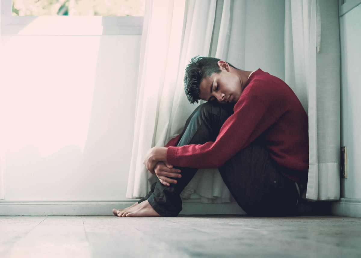 man hugging his legs and sitting on the floor with closed eyes