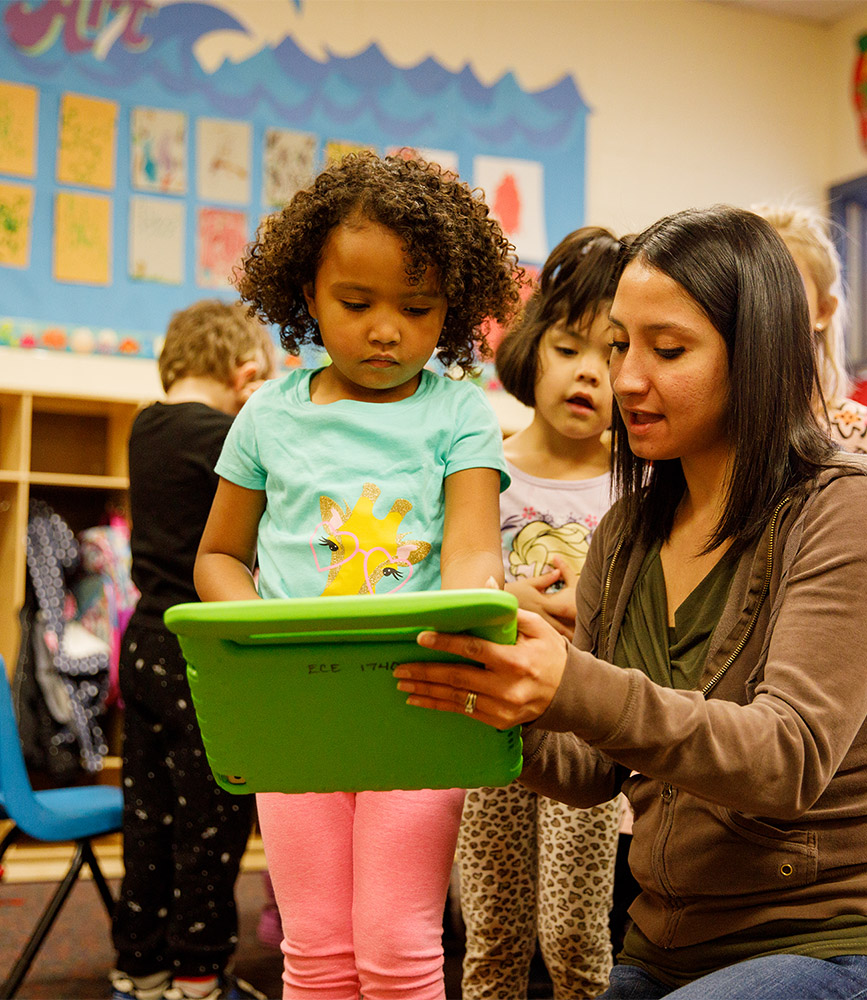 An early childhood educator explains how a miniature smartboard works to a young child.