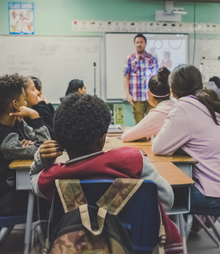 teacher stands at the head of the class as students look on enraptured