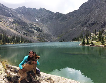 Betzabe Karagozian poses for a photo with her dog in front of a mountain lake