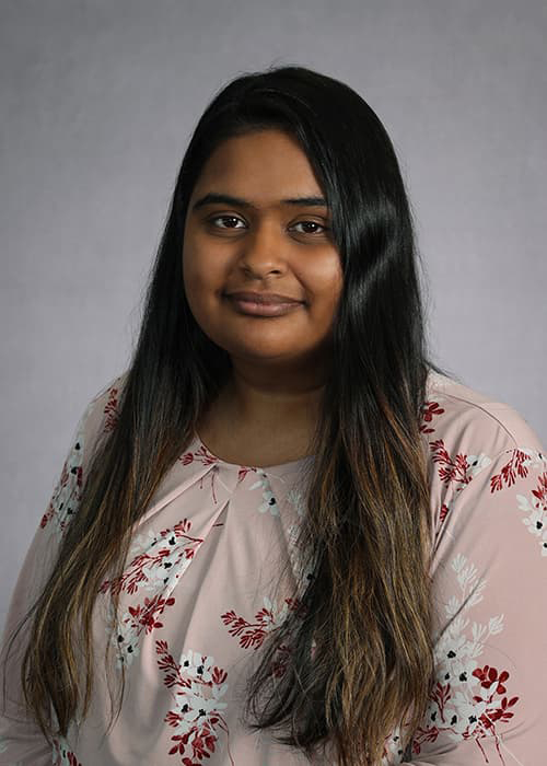 Sabha Daniel in a floral blouse and long brown hair, smiling in to the camera.