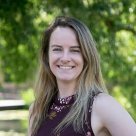 Anna Linn with long blonde hair standing outside and smiling with her teeth.