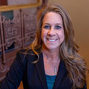 Jaime McMullen Garcia in a black blazer and long brown-blonde hair, smiling with her teeth.