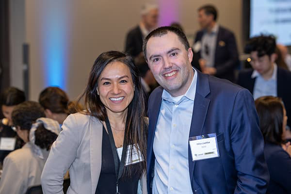 Mike Liedke in a blue suite smiling with his teeth, arm-in-arm with a student in a tan jacket and long dark hair, also smiling with her teeth.