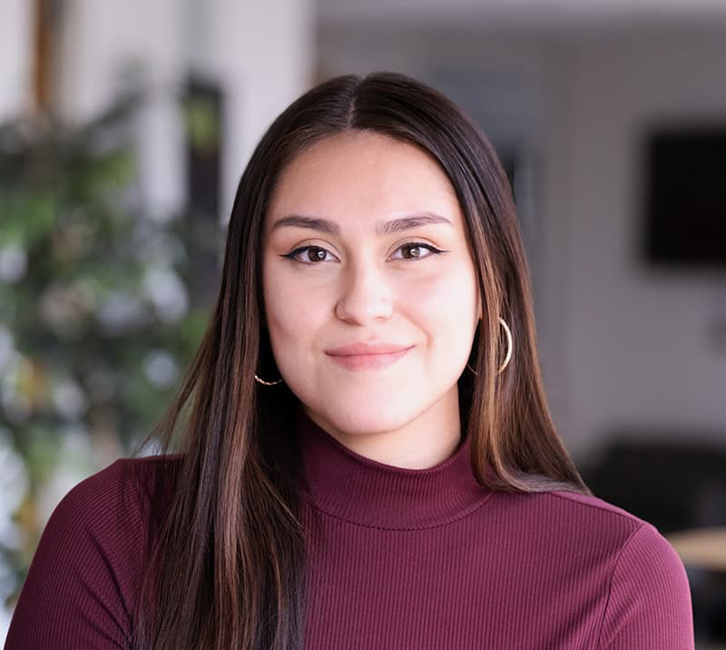 Mariely Marquez-Lopez  in a burgundy blouse, long brown hair, and hooped earrings smiling at the camera.