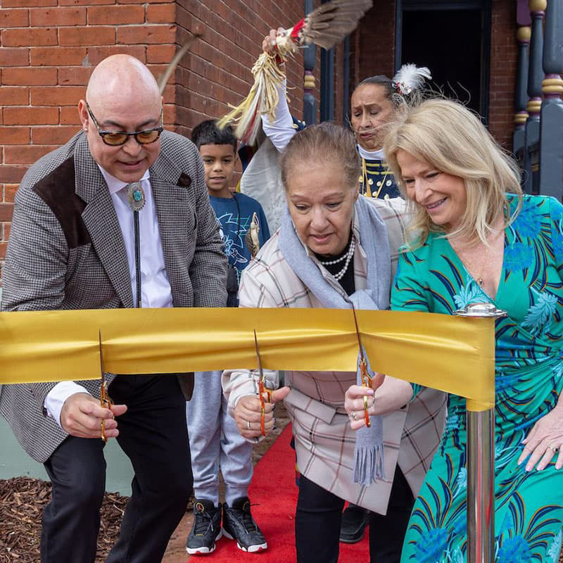 Group of people cutting a large gold ribbon in front of a house.