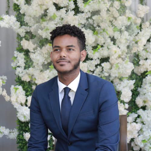 Abel Mesfin in a blue suit with white flowers behind him.