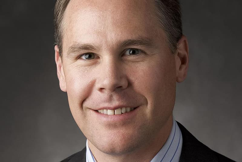 Close-up image of Case Lozar in a suit smiling with his teeth.