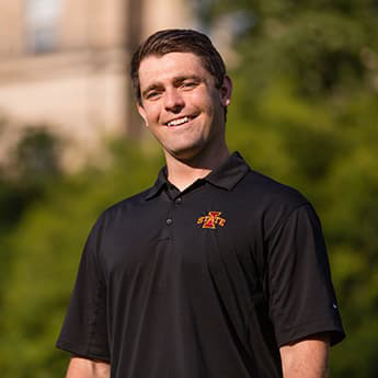 Jordan Arellanes wearing a black polo shirt, short brown hair, and smiling with his teeth.