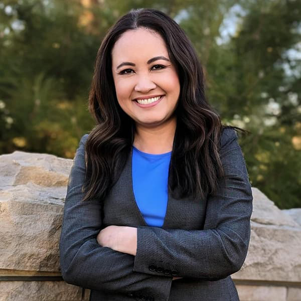 Headshot of Nga Vương-Sandoval in a blue blouse and gray suit jacket with long brown hair smiling with her teeth.