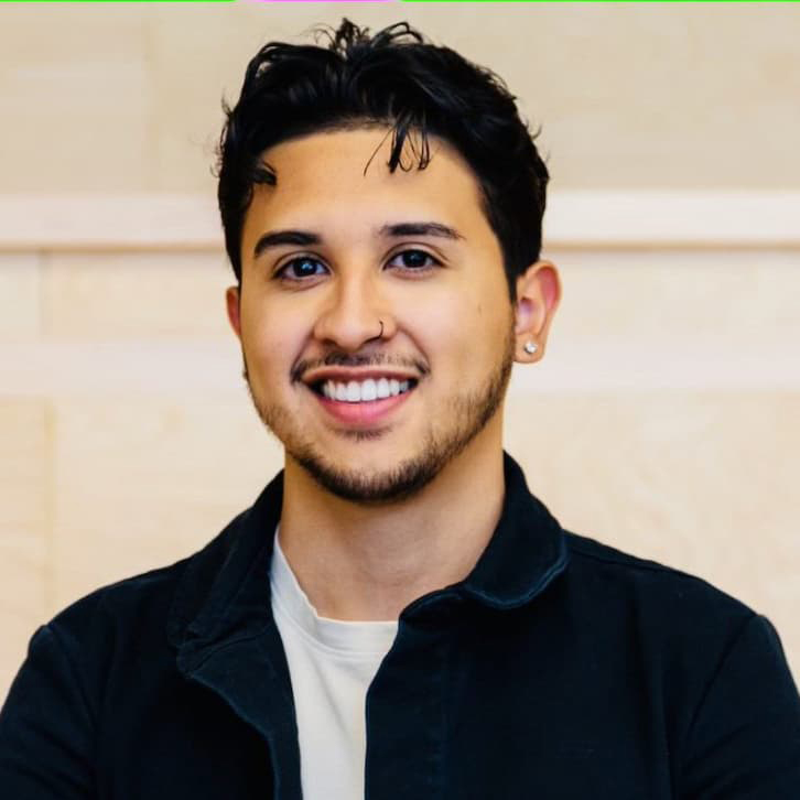 Oscar Fraire from the shoulders up smiling, wearing a dark jacket with black hair, ear and nose piercings.