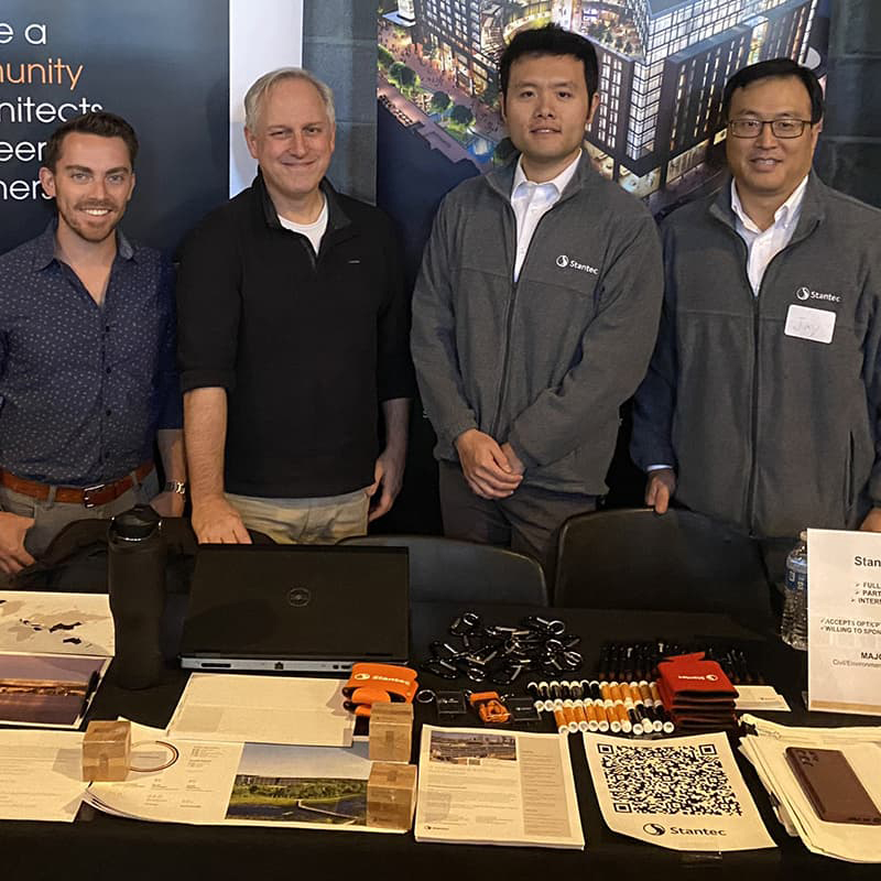 Brandon Zhou with three other students standing behind a table that shows their research work.