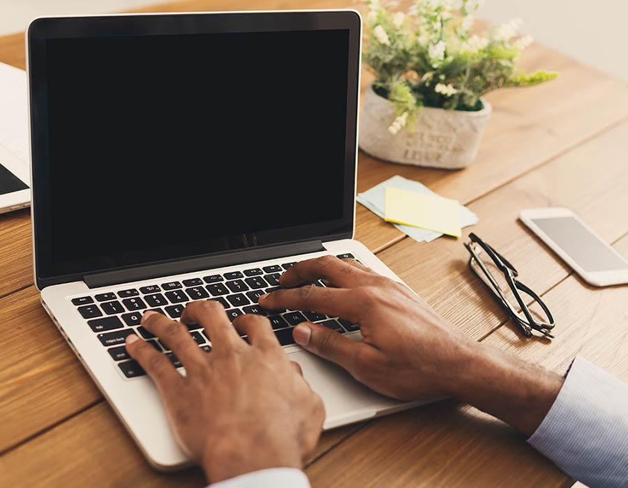 View of a man's hands typing on a laptop.