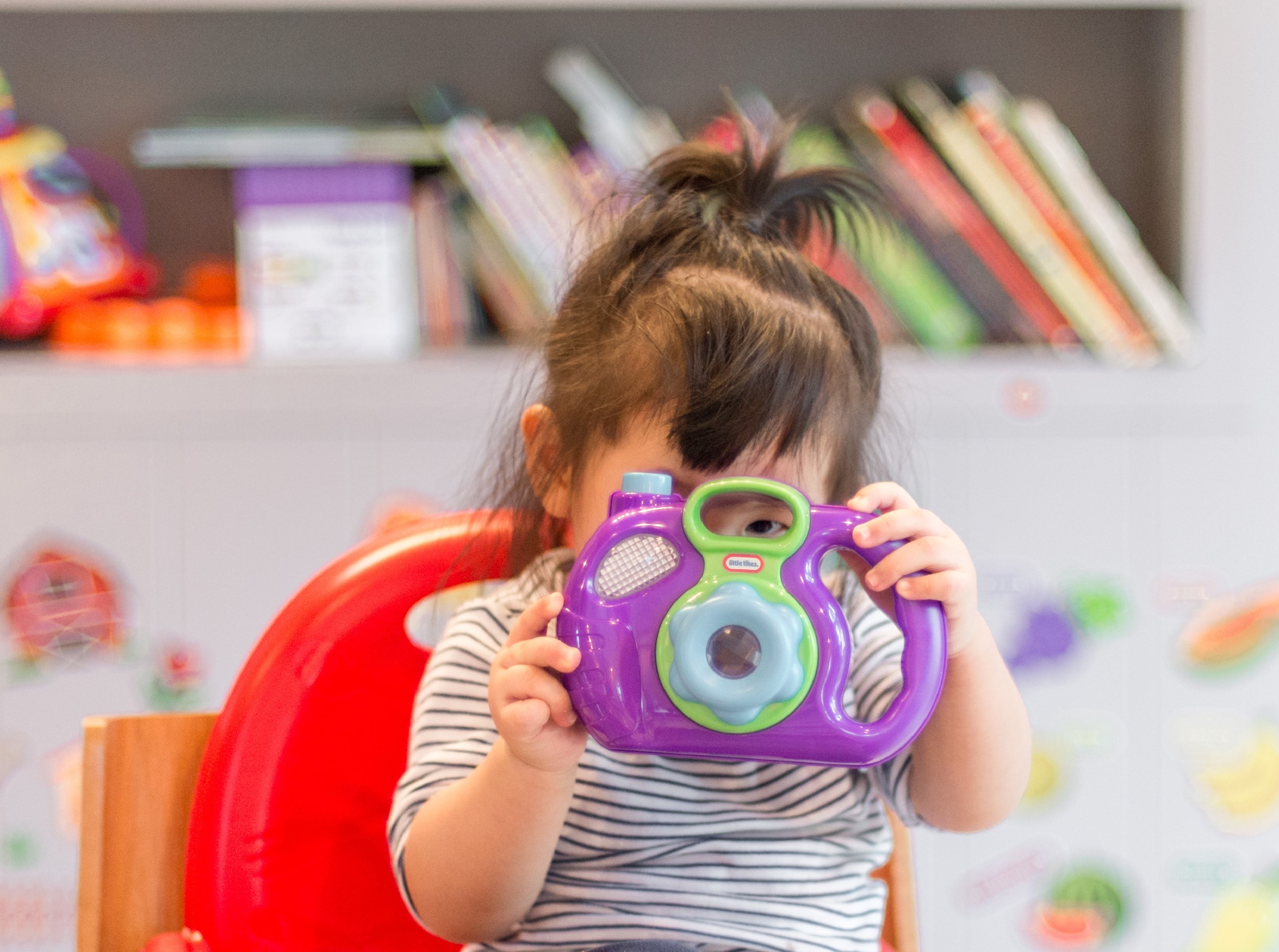 Young girl points purple toy camera at viewer.