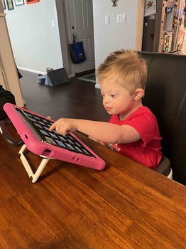 Young child using index finger to select icon on assistive communication device